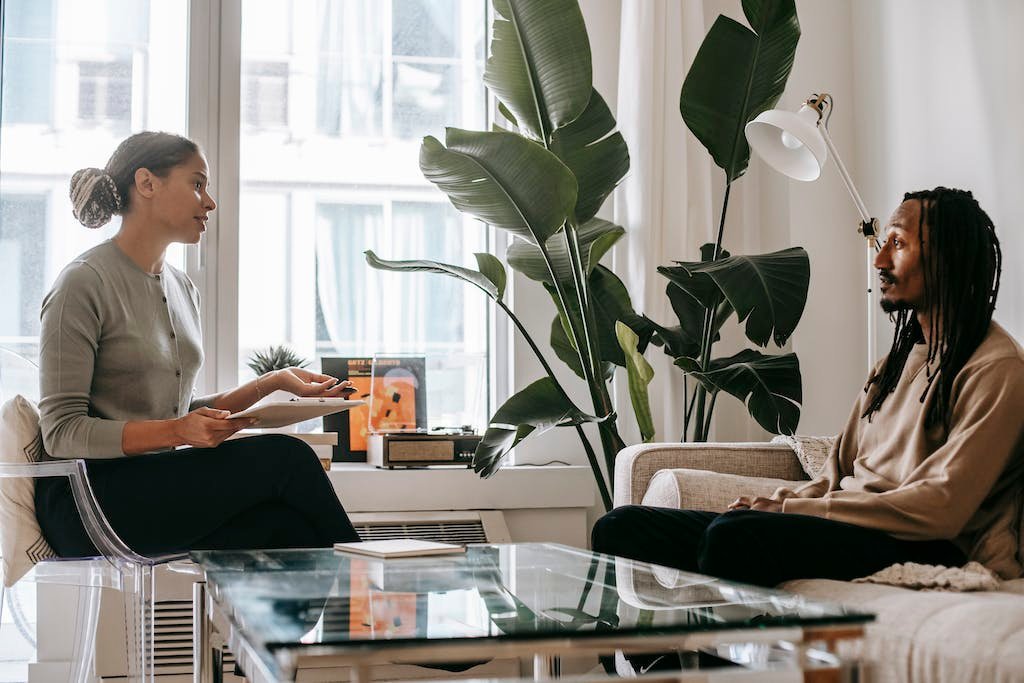 Side view of professional female African American therapist sitting in front of black male patient during psychotherapy session in office to show recovery