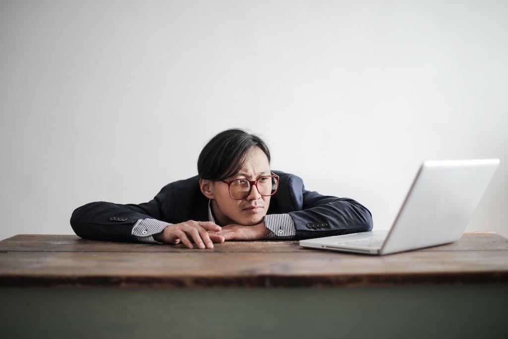 Bored formal man watching laptop at desk researching what to expect from a recovery coach